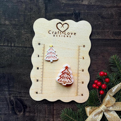 Two sizes of a folk art Christmas tree clay design displayed on a Craft Love Designs wooden measuring board. The tree features symmetrical floral, leaf, dot, and ornamental details with a star topper.