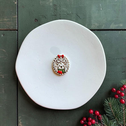 Finished Christmas reindeer piece centered on a white plate, featuring a small deer with antlers and scarf inside an oval woodland frame topped with a red bow, with evergreen and red berries nearby