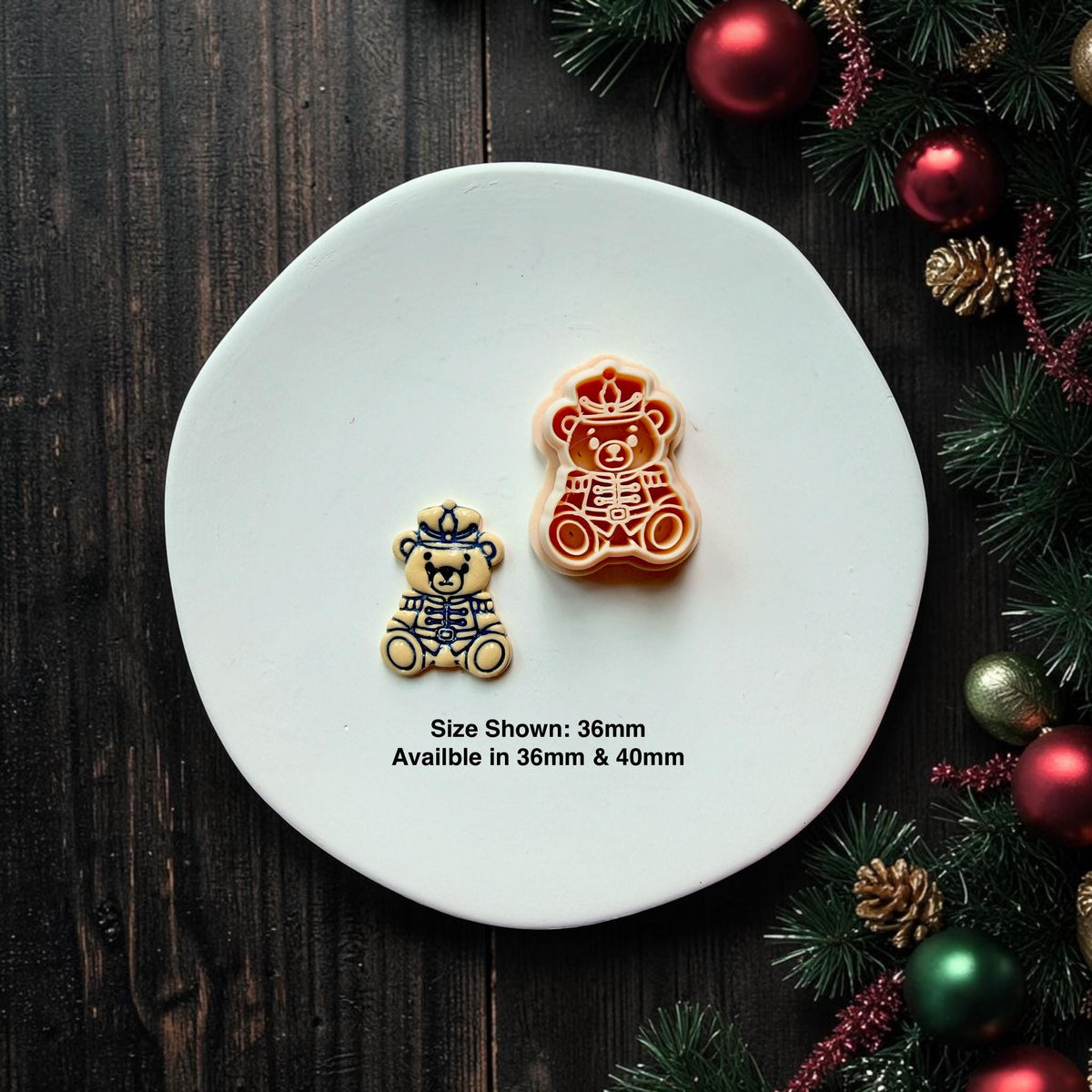 Finished nutcracker teddy bear clay piece beside the matching larger design on a white plate with Christmas greenery and ornaments; text states size shown is 36mm and available sizes are 36mm and 40mm.