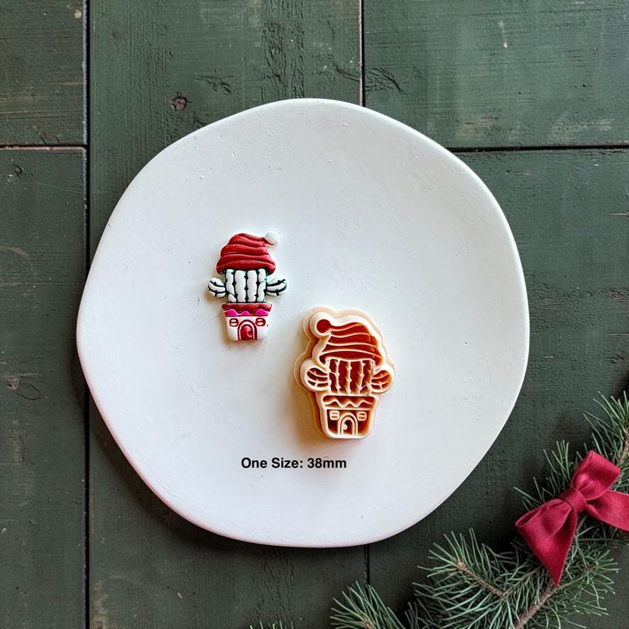 Finished colorful Christmas cactus clay piece beside the matching cutter on a white plate, with text showing one size at 38mm and a red bow with evergreen branch nearby.