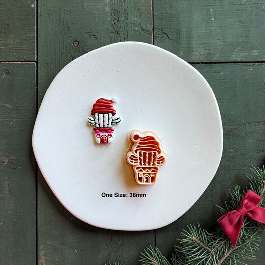 Finished colorful Christmas cactus clay piece beside the matching cutter on a white plate, with text showing one size at 38mm and a red bow with evergreen branch nearby.