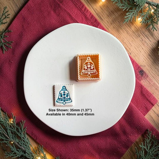 Decorative Christmas bell polymer clay cutter beside the finished white bell clay piece on a white plate, with text showing the 35mm size pictured and availability in 40mm and 45mm.