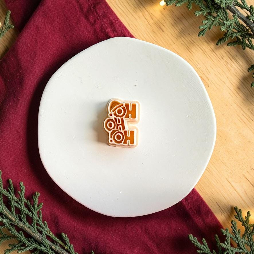 Ho Ho Ho polymer clay cutter centered on a white plate, showing the stacked Christmas phrase with a Santa hat detail incorporated into the design.