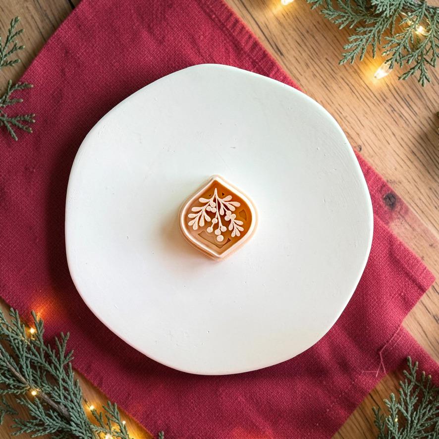 Mistletoe polymer clay cutter centered on a white plate, showing the pointed ornamental outer shape with leafy botanical branches and berry details inside.