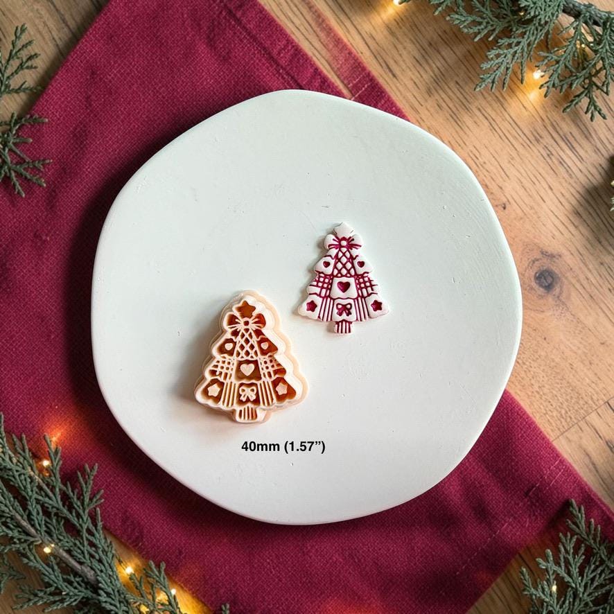 Finished decorative Christmas tree clay piece beside the matching polymer clay cutter on a white plate, showing heart, bow, lattice, and striped details with text indicating a 40mm or 1.57 inch size.
