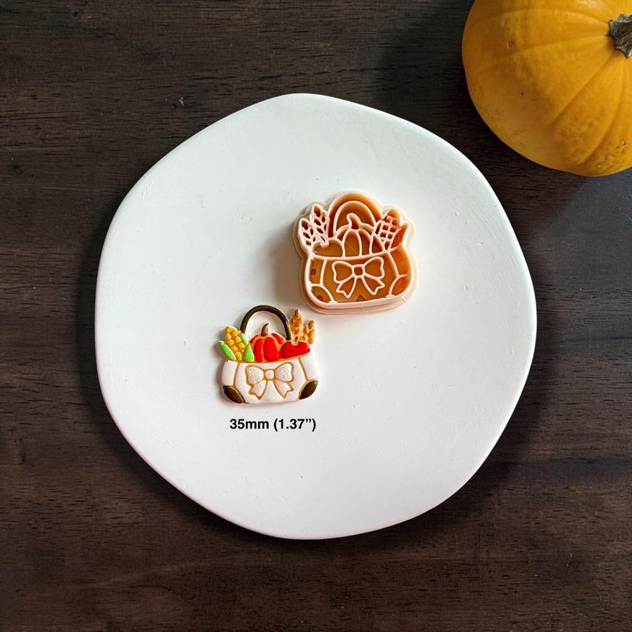 Fall harvest market bag polymer clay cutter beside the finished colorful clay piece on a white plate, with text showing the 35mm size and a small orange pumpkin in the background.