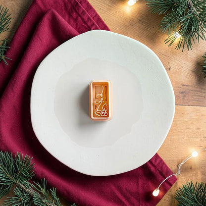 Joy and holly polymer clay cutter centered on a white plate, showing the slim rectangular shape with script lettering and holly leaves with berry details.