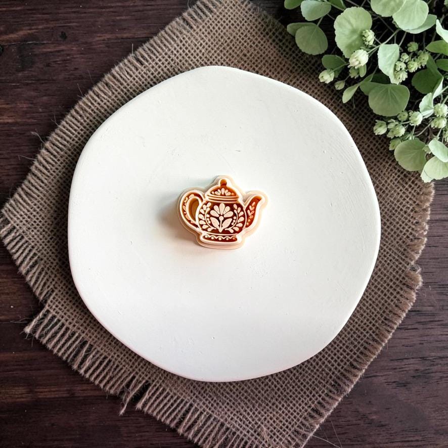 Folk teapot polymer clay cutter centered on a white plate, showing the teapot shape with floral and ornamental interior details.
