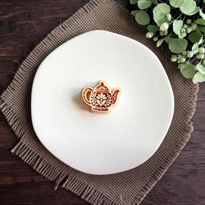 Folk teapot polymer clay cutter centered on a white plate, showing the teapot shape with floral and ornamental interior details.